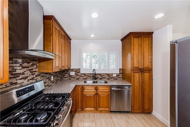 kitchen with appliances with stainless steel finishes, brown cabinets, a sink, wall chimney range hood, and backsplash