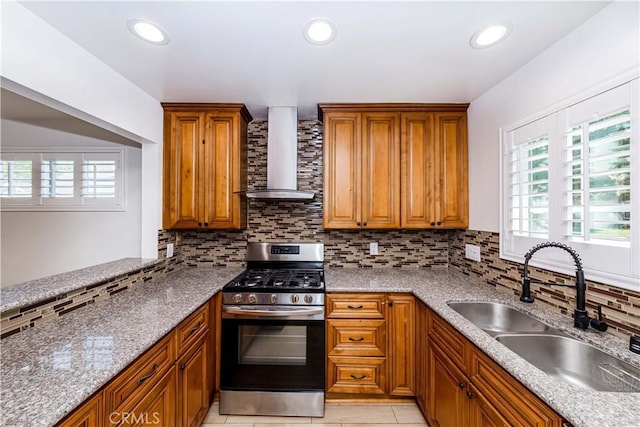 kitchen with stainless steel gas range oven, a sink, backsplash, wall chimney exhaust hood, and brown cabinetry