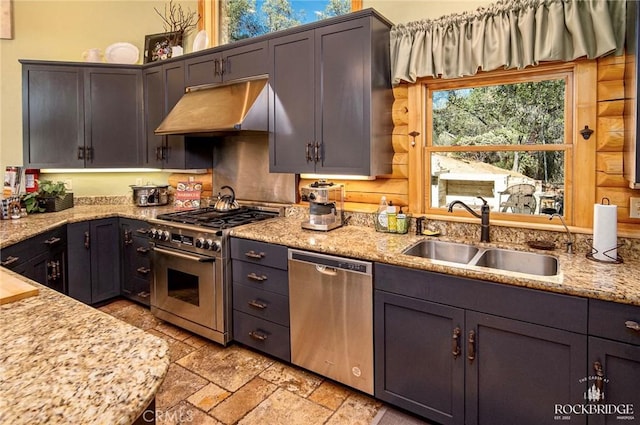 kitchen featuring appliances with stainless steel finishes, light stone counters, stone tile flooring, under cabinet range hood, and a sink