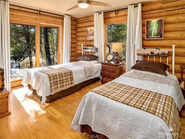 bedroom with access to outside, multiple windows, log walls, and wood finished floors