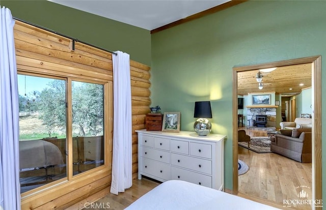 bedroom featuring a stone fireplace, rustic walls, and wood finished floors