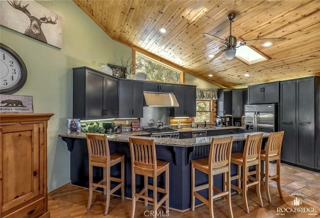 kitchen featuring wooden ceiling, under cabinet range hood, a peninsula, appliances with stainless steel finishes, and dark stone countertops