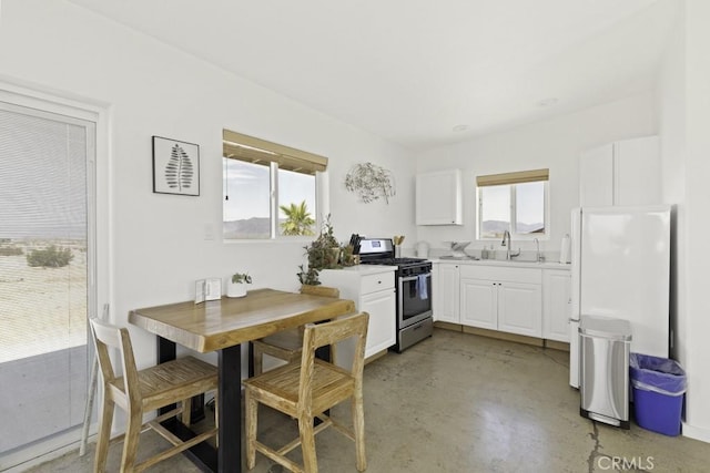 kitchen with finished concrete flooring, white cabinets, freestanding refrigerator, stainless steel gas range, and a sink