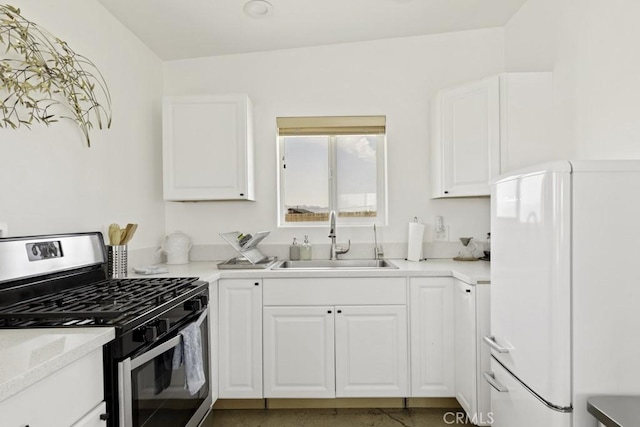 kitchen with stainless steel range with gas stovetop, freestanding refrigerator, light countertops, white cabinetry, and a sink