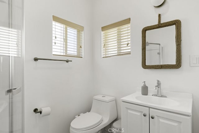 bathroom featuring a shower with shower door, vanity, and toilet