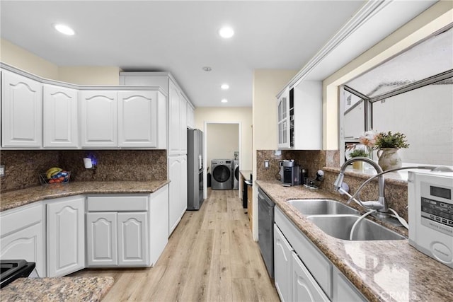 kitchen featuring appliances with stainless steel finishes, washer and dryer, white cabinets, and a sink