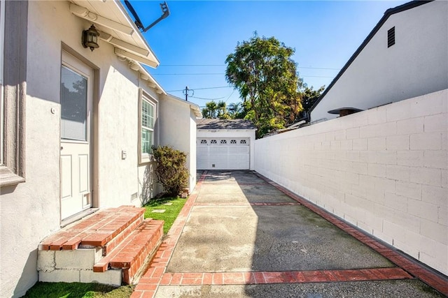 view of side of home with driveway, a detached garage, fence, an outdoor structure, and stucco siding