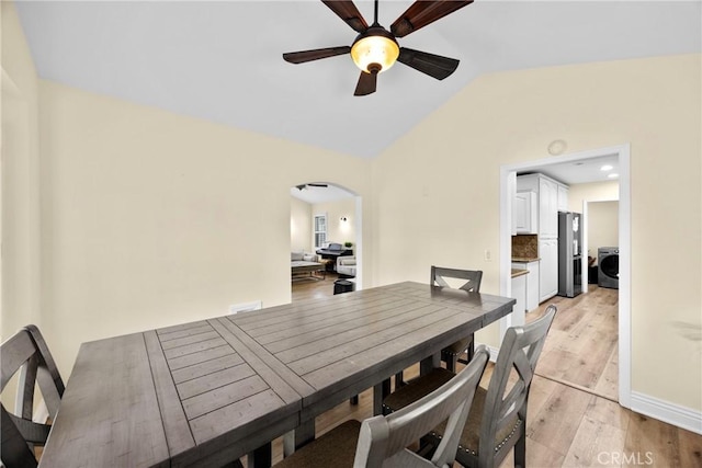 dining room with light wood finished floors, arched walkways, ceiling fan, washer / clothes dryer, and vaulted ceiling