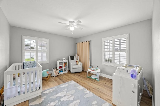 bedroom featuring a crib, multiple windows, baseboards, and wood finished floors