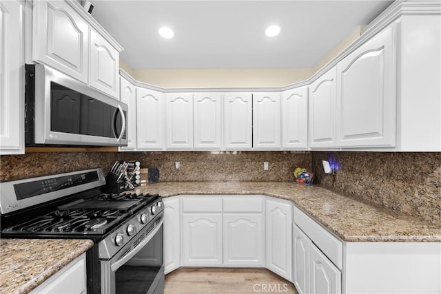 kitchen with stainless steel appliances, white cabinetry, backsplash, and light stone countertops