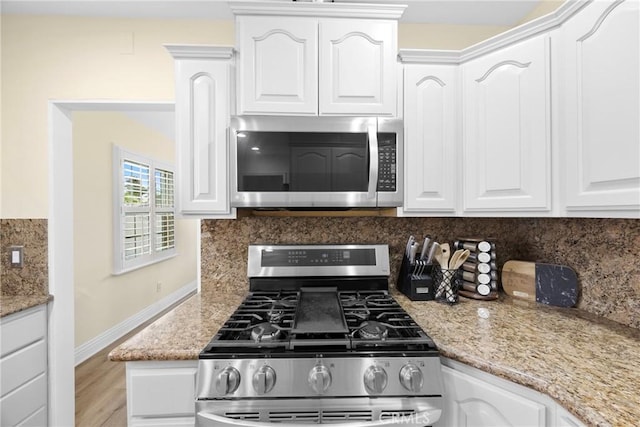 kitchen featuring stainless steel appliances, white cabinetry, backsplash, and light stone countertops