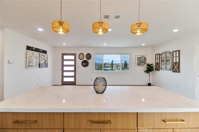 kitchen featuring visible vents, brown cabinetry, hanging light fixtures, light stone countertops, and recessed lighting