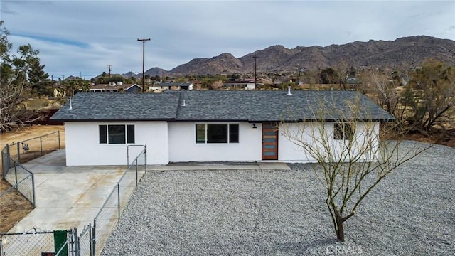 exterior space featuring stucco siding, fence, a mountain view, and roof with shingles