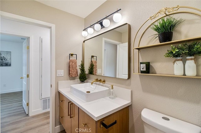 half bath featuring visible vents, toilet, vanity, wood finished floors, and baseboards