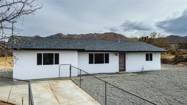 view of front of home with a shingled roof, fence, a mountain view, and stucco siding