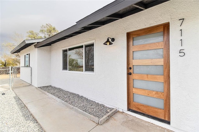 entrance to property featuring fence, a gate, and stucco siding