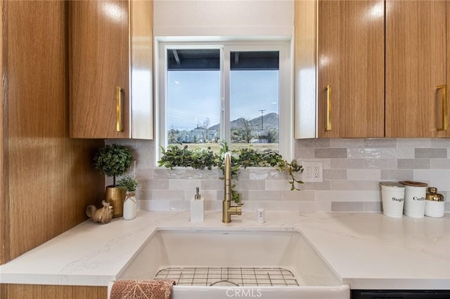 kitchen with brown cabinetry, a sink, backsplash, and light stone countertops