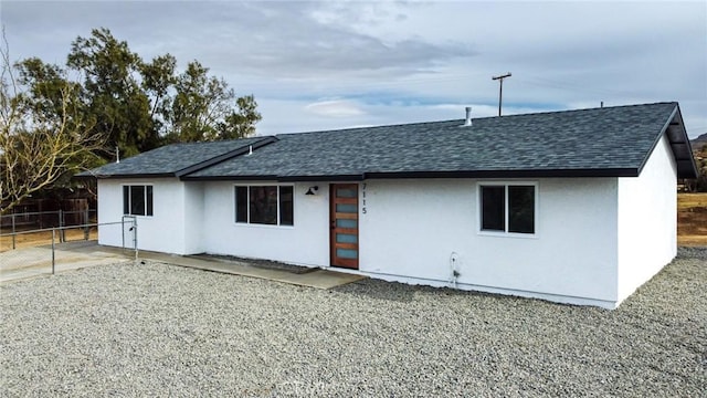 rear view of house with a shingled roof, fence, and stucco siding