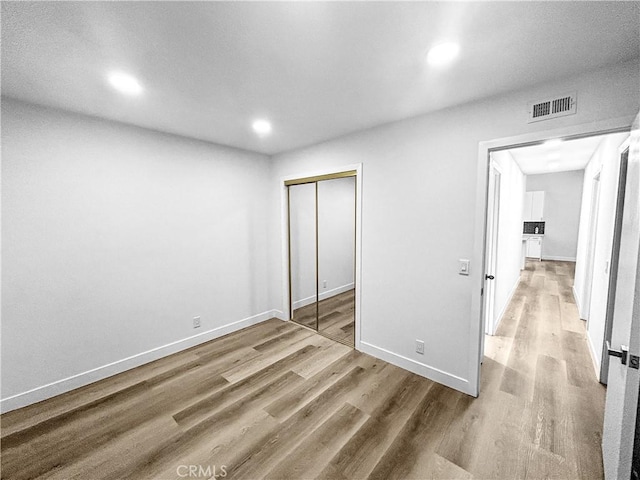 unfurnished bedroom featuring baseboards, a closet, visible vents, and wood finished floors