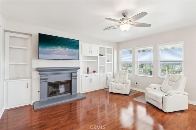 sitting room with a glass covered fireplace, built in shelves, wood finished floors, and baseboards