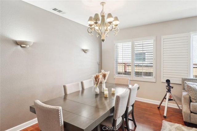 dining space featuring wood finished floors, visible vents, a chandelier, and baseboards