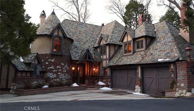 tudor house featuring brick siding, a chimney, stucco siding, a high end roof, and driveway