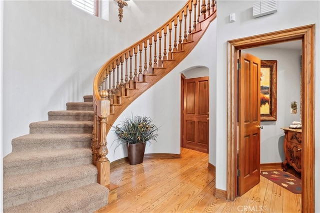 stairs with arched walkways, baseboards, and hardwood / wood-style floors