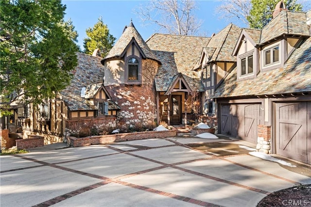 english style home featuring stone siding, a high end roof, concrete driveway, and stucco siding