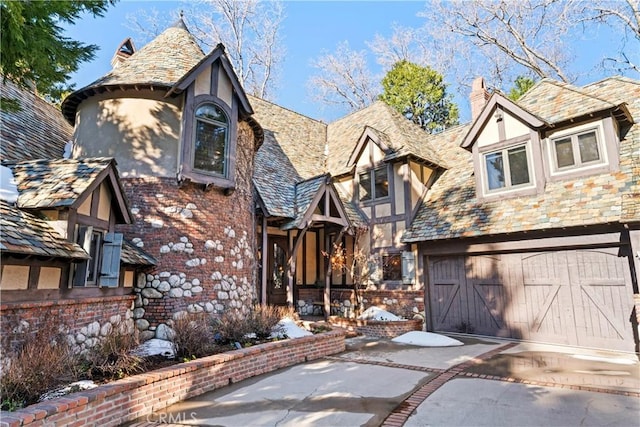 tudor home with brick siding, a chimney, stucco siding, a garage, and a high end roof