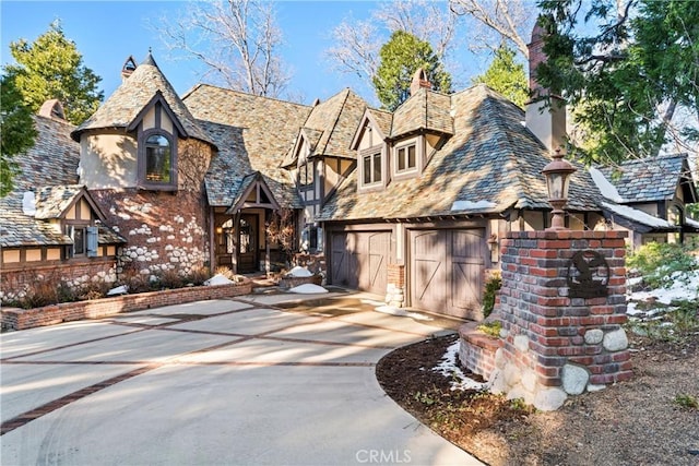 tudor house featuring a garage, concrete driveway, a chimney, a high end roof, and stucco siding