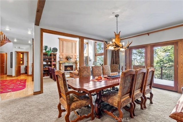 dining area featuring a wealth of natural light, an inviting chandelier, a high end fireplace, and light colored carpet