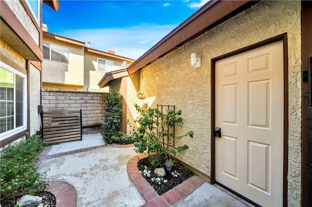 property entrance with stucco siding, a patio, and fence