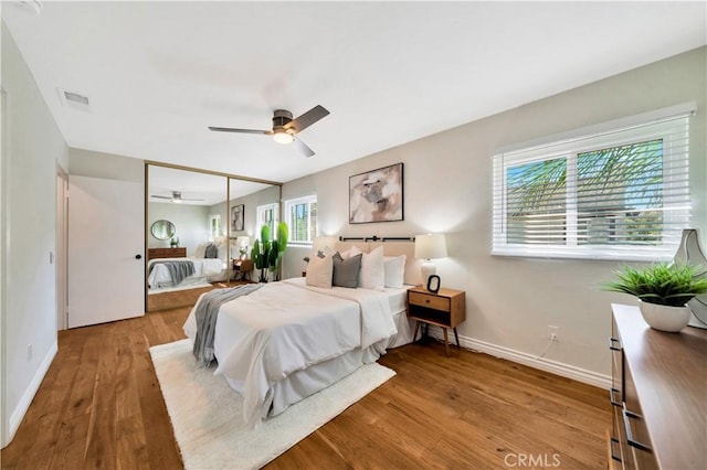 bedroom featuring a ceiling fan, visible vents, wood finished floors, baseboards, and a closet