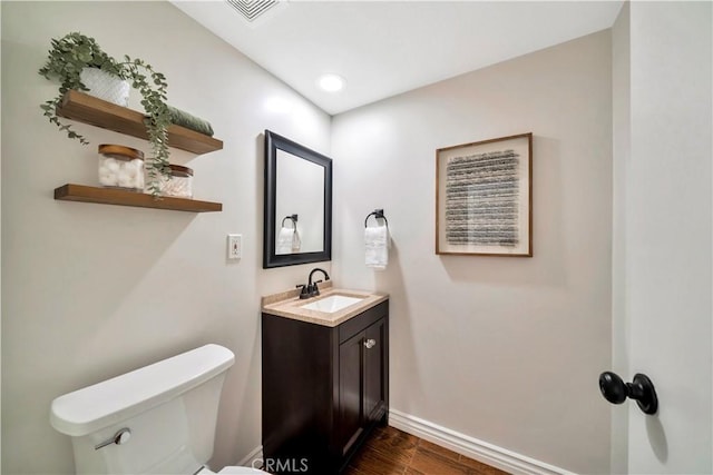 half bathroom with visible vents, toilet, wood finished floors, baseboards, and vanity