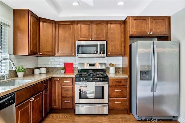 kitchen featuring a sink, light stone counters, tasteful backsplash, wood finished floors, and stainless steel appliances