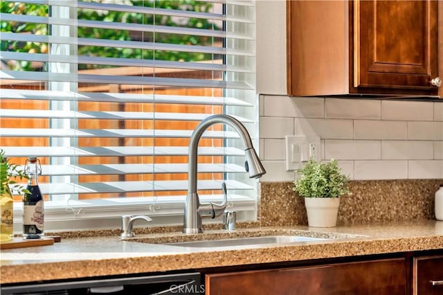 room details with a sink, dishwashing machine, light stone counters, and backsplash