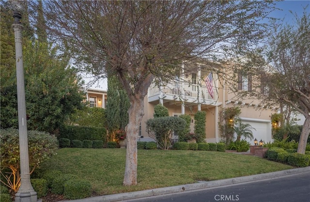 obstructed view of property with a garage, a balcony, a front lawn, and stucco siding