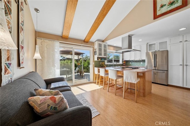 kitchen with island exhaust hood, a breakfast bar area, lofted ceiling with beams, glass insert cabinets, and freestanding refrigerator