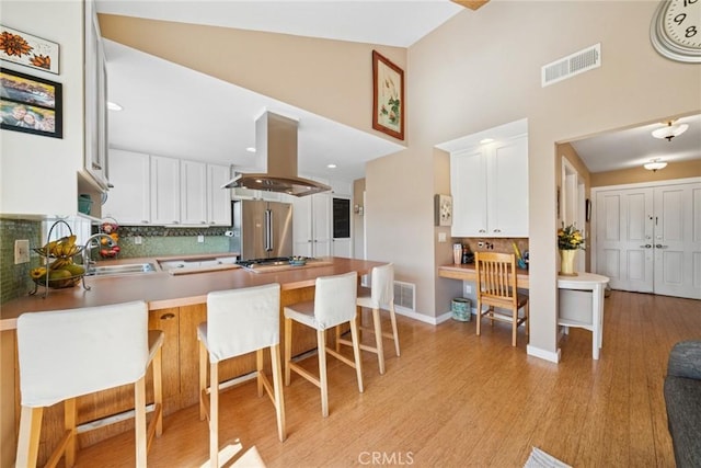 kitchen featuring stainless steel appliances, a peninsula, a sink, visible vents, and island exhaust hood