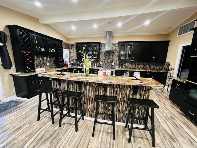 bar with visible vents, light wood-style flooring, gas stove, wall chimney range hood, and wet bar