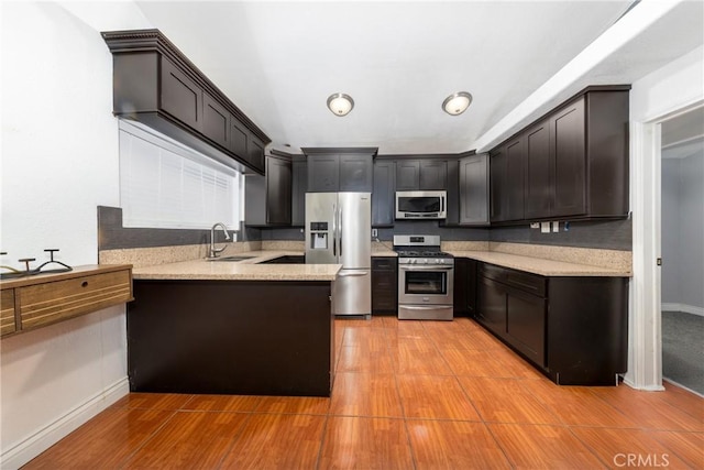 kitchen featuring appliances with stainless steel finishes, baseboards, a peninsula, and a sink