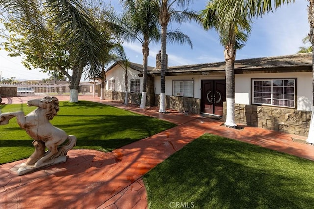 ranch-style house with stucco siding, stone siding, a front yard, and fence