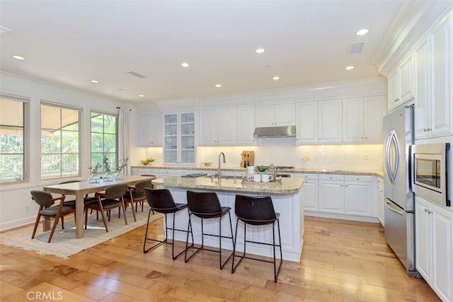 kitchen featuring light wood finished floors, under cabinet range hood, white cabinetry, and a sink