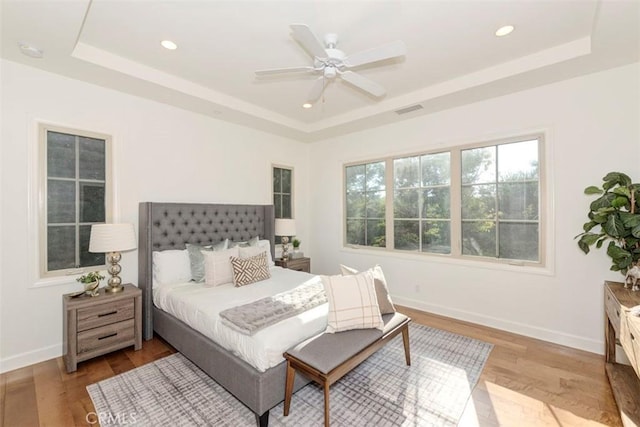 bedroom featuring light wood finished floors, a tray ceiling, visible vents, and baseboards