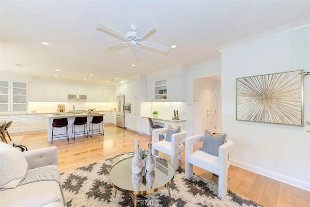 living room featuring baseboards, ceiling fan, ornamental molding, light wood-style floors, and recessed lighting