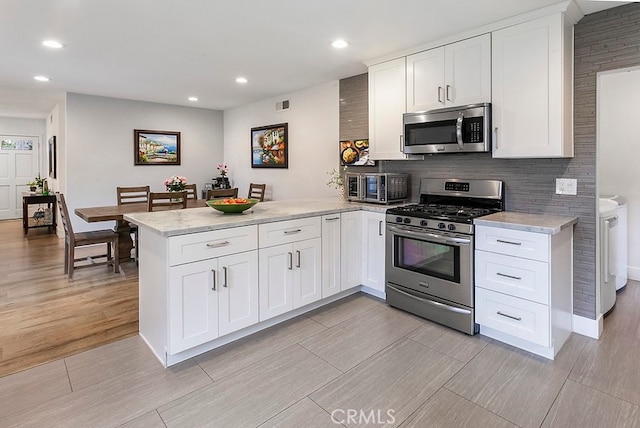 kitchen featuring stainless steel appliances, a peninsula, visible vents, white cabinets, and washing machine and clothes dryer