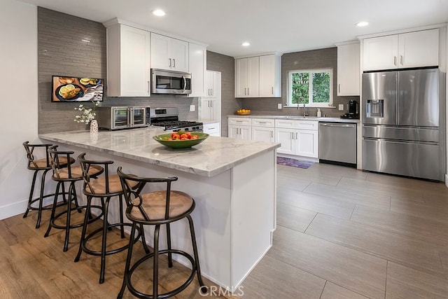 kitchen featuring white cabinets, appliances with stainless steel finishes, a peninsula, a sink, and backsplash