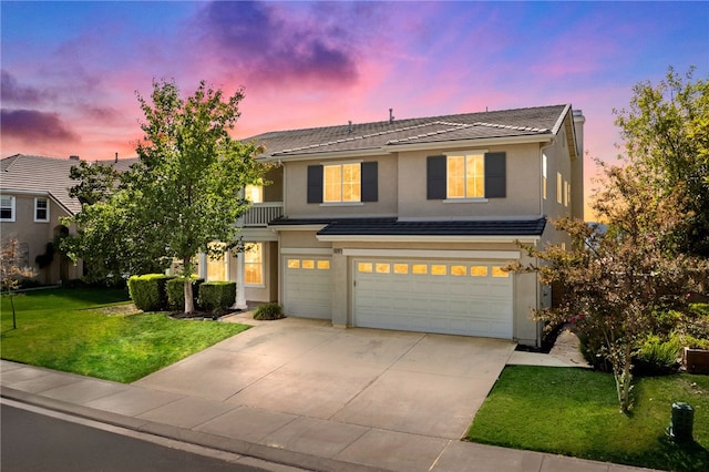 traditional home featuring a garage, concrete driveway, a tile roof, a yard, and stucco siding