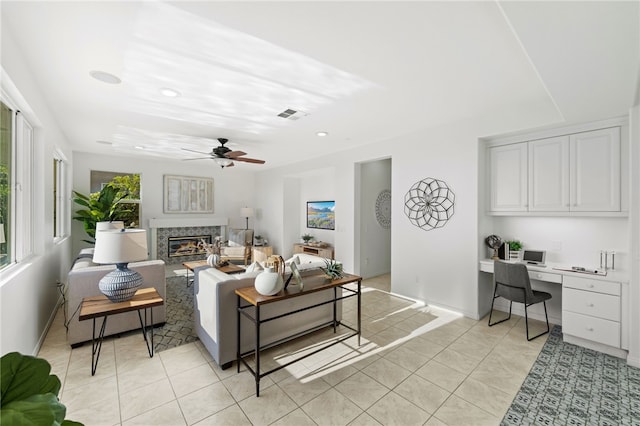 living room with visible vents, a ceiling fan, a glass covered fireplace, built in desk, and light tile patterned flooring