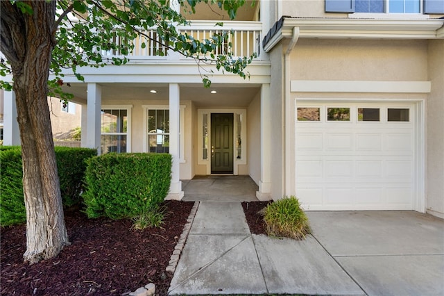 doorway to property featuring a balcony, an attached garage, concrete driveway, and stucco siding